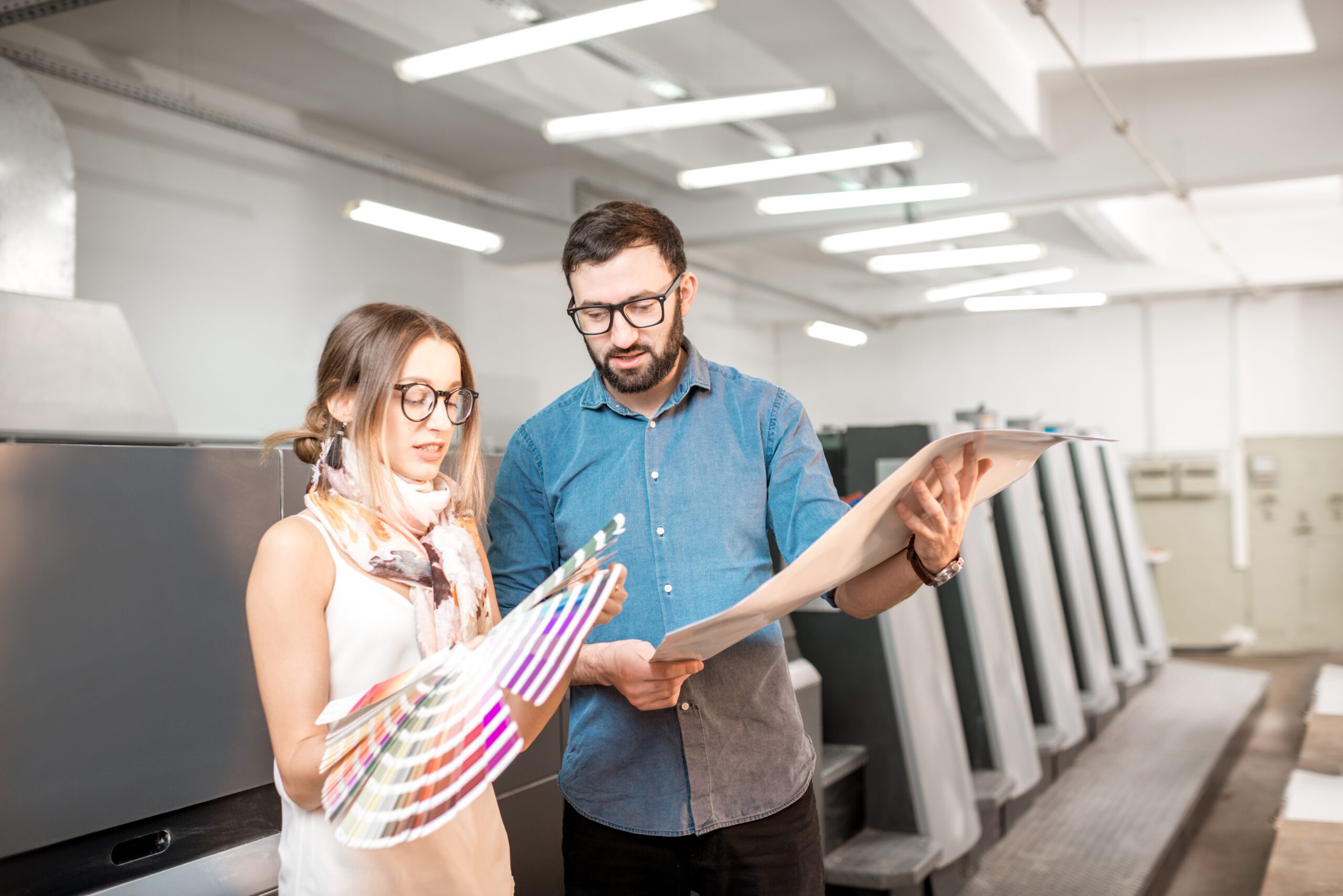 Young,Woman,Designer,And,Print,Operator,Working,Together,With,Color Young woman designer and print operator working together with color swatches standing at the print manufacturing